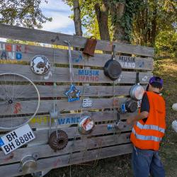 Junge in Warnweste steht vor Bretterwand mit diversen Metallteilen